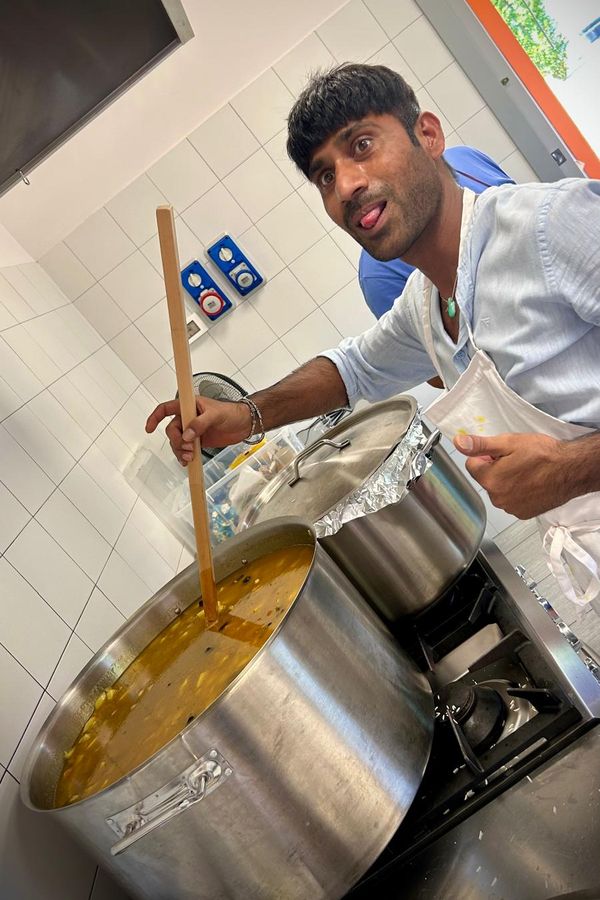 Un cuoco gira il pentolone con un lungo mestolo di legno e fa una smorfia all'obiettivo.