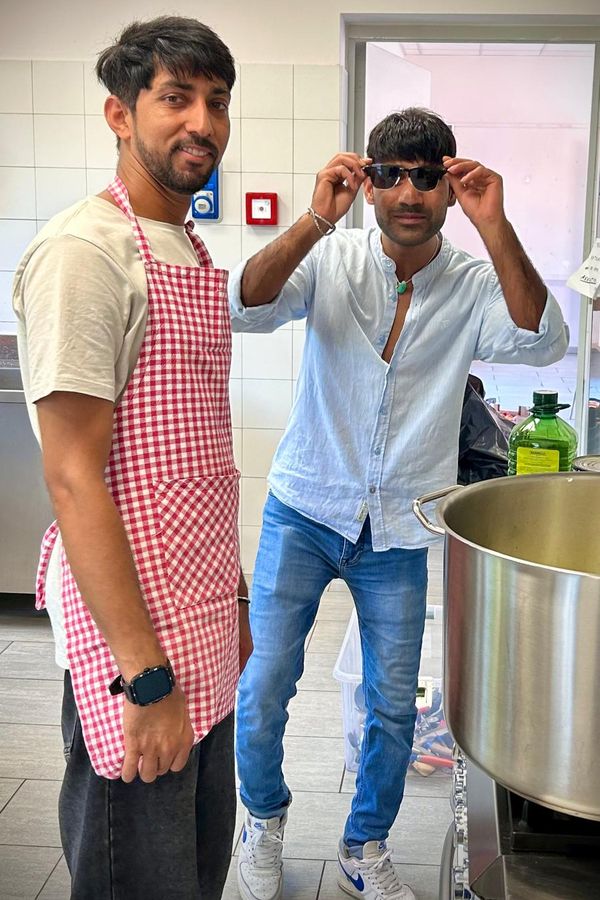 Due ragazzi in cucina: uno col grembiule a quadretti, l'altro si sistema gli occhiali da sole.