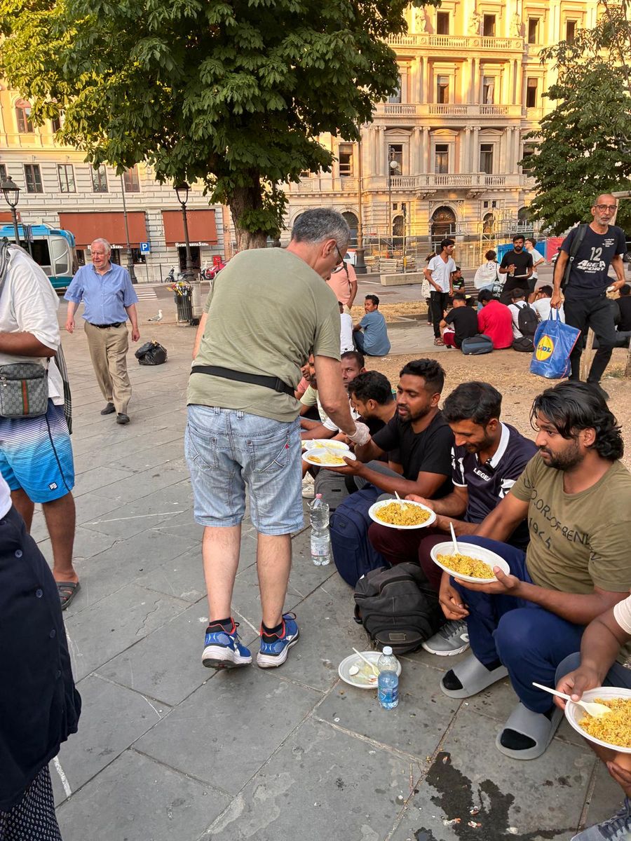 Un volontario porge un piatto di riso ai ragazzi seduti in piazza, davanti ai palazzi di Trieste.